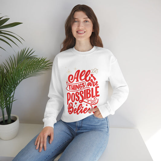 A woman wearing a cozy white sweatshirt , featuring the uplifting slogan "All Things Are Possible If You Believe" printed across the front in red bold font. This sweatshirt blends motivation with style, perfect for everyday wear.