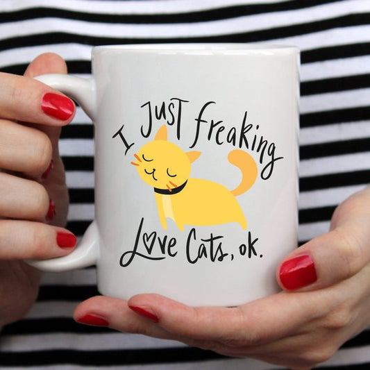 White ceramic mug with the playful text "I Just Freaking Love Cats OK" printed in bold black font. A fun, inspirational mug for cat lovers, perfect for coffee or tea, with a simple and stylish design.