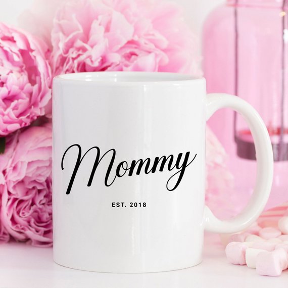 A white ceramic mug with the text "Mom Est. 2018" printed in an elegant black font, designed as a meaningful keepsake and gift for mothers.