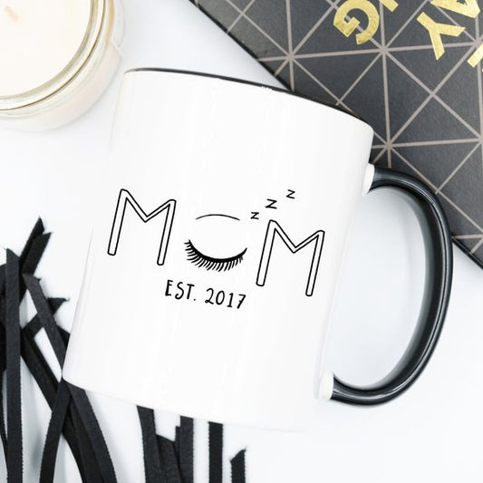 White ceramic mug with the words "Mom Est. 2017" printed in elegant black lettering, symbolizing the year of becoming a mom. Perfect for everyday use or as a thoughtful gift for mothers.